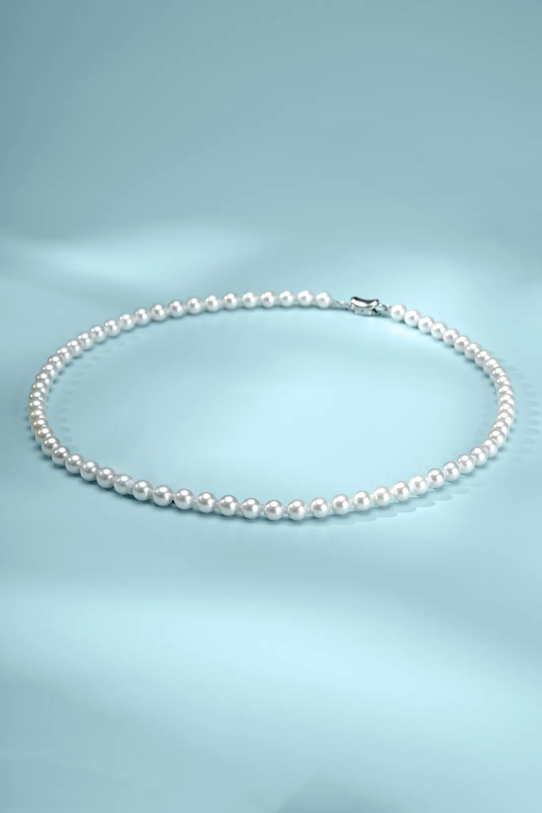 A very even strand of small white round pearls laid on blue fabric