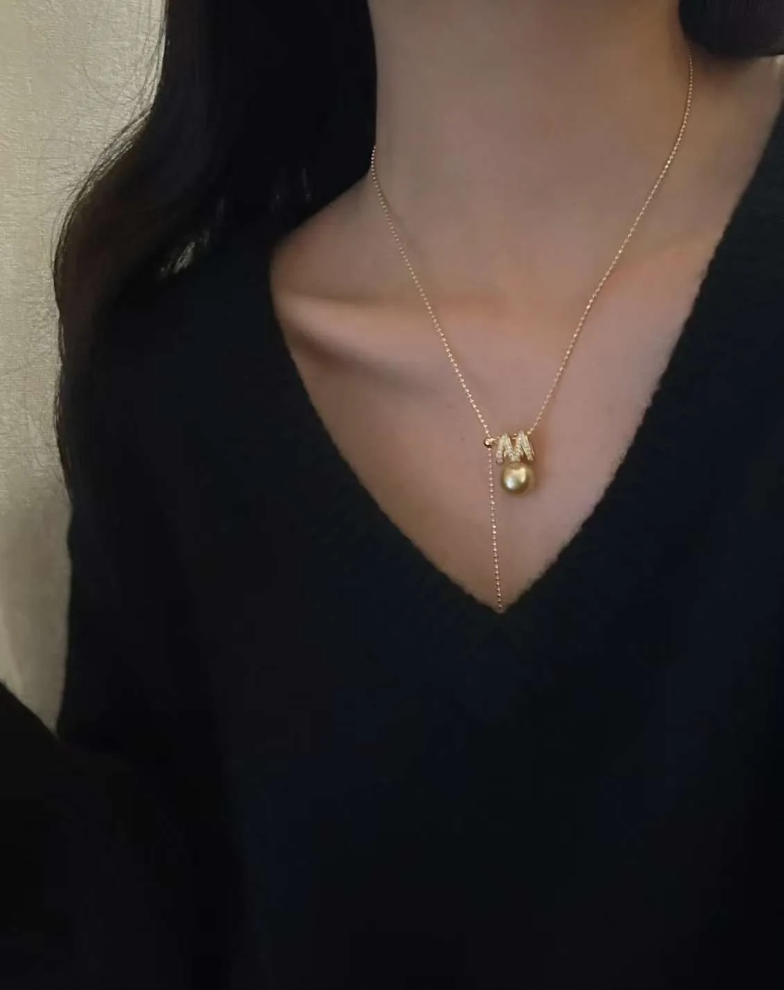 A small golden pearl pendant worn on a fine chain with a black top