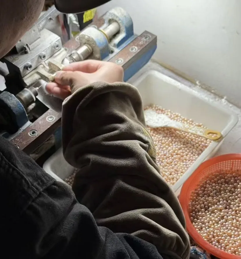 A worker drilling light pink pearls, with a tray of pearls waiting beside the machine