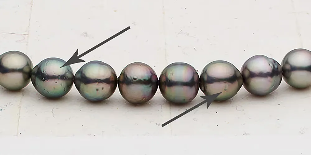 Dark pearls on a strand with arrows indicating small surface marks