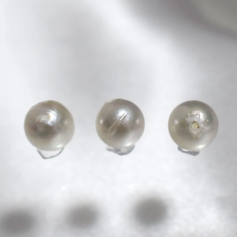 Three white pearls showing a smooth face, a surface line, and a small pit near the drill hole