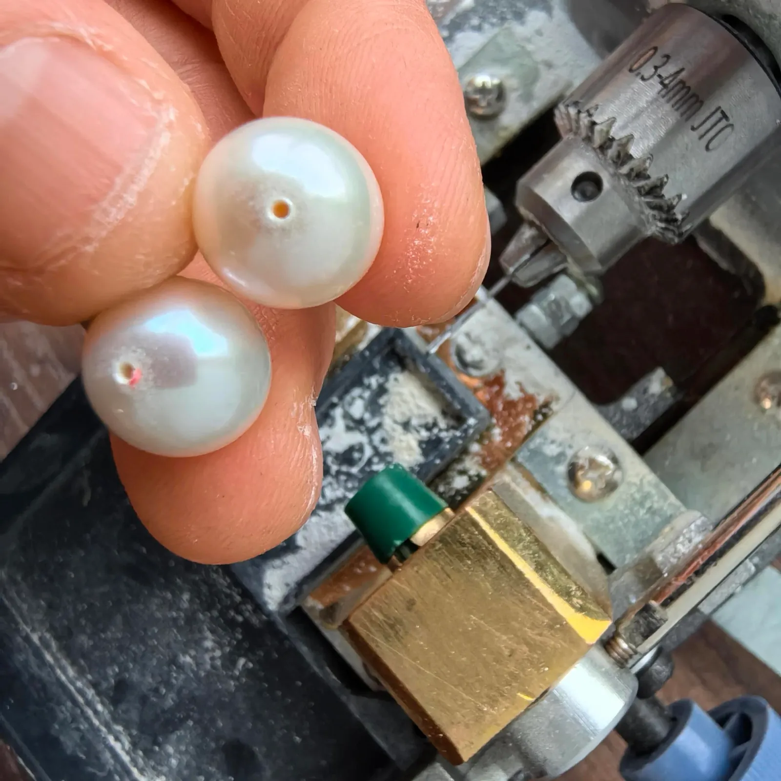 White cultured pearls with small drill holes held beside a pearl drilling machine