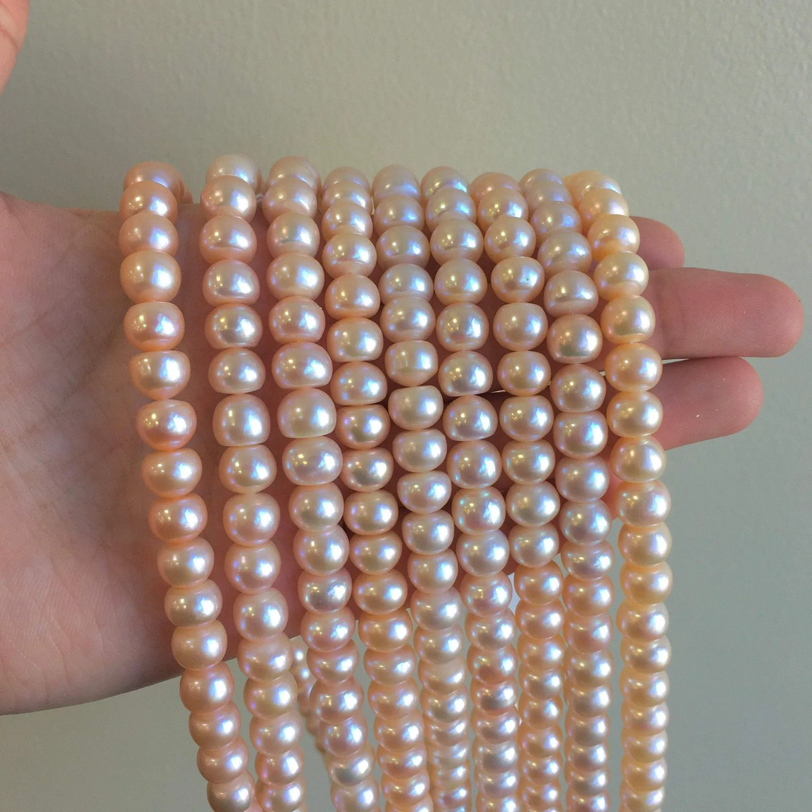 Peach freshwater pearl strands held in a hand, showing rounded faces